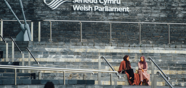 Dau berson yn eistedd ar risiau llechfaen adeilad y Senedd.