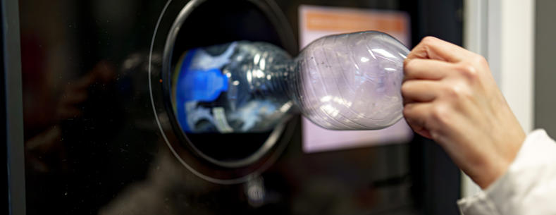 Someone putting a plastic bottle into a deposit return take-back point.