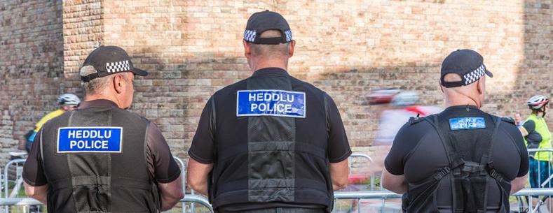 Tri heddwas yn sefyll â'u cefnau i'r camera