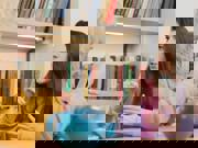 Dwy fenyw yn eistedd wrth fwrdd gyda phot o de, yn cael sgwrs drwy ddefnyddio Iaith Arwyddion Prydain.