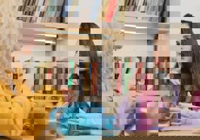 Dwy fenyw yn eistedd wrth fwrdd gyda phot o de, yn cael sgwrs drwy ddefnyddio Iaith Arwyddion Prydain.