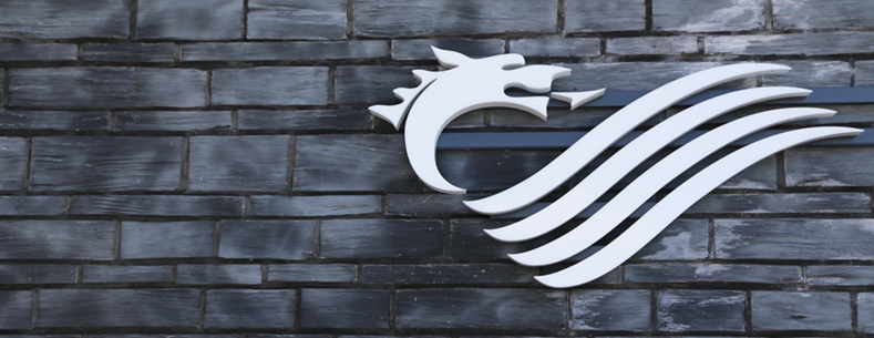 Logo ar adeilad y Senedd gyda wal o lechi