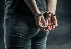 Person mewn gefynnau â’i ddwylo y tu ôl i’w gefn 