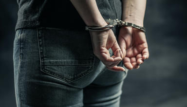 Person mewn gefynnau â’i ddwylo y tu ôl i’w gefn 