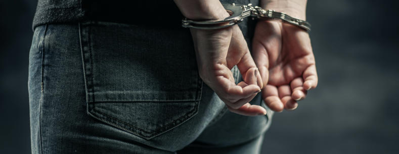 Person mewn gefynnau â’i ddwylo y tu ôl i’w gefn 