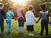 Plant yn chwarae yn yr awyr agored ar ardal laswelltog, gyda sawl plentyn yn rhedeg ac yn rhyngweithio mewn lleoliad tebyg i barc o dan olau naturiol.