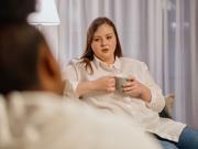 Menyw yn dal diod yn eistedd gyferbyn â pherson arall 