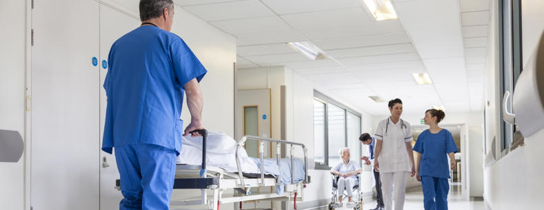 Llun o staff gofal iechyd yn gwthio gwely ysbyty gwag