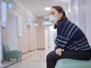 Woman sitting alone in a hospital corridor with a face mask on