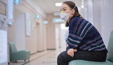 Woman sitting alone in a hospital corridor with a face mask on