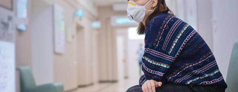 Woman sitting alone in a hospital corridor with a face mask on