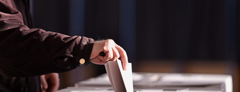 llaw yn rhoi papur pleidleisio mewn blwch pleidleisio