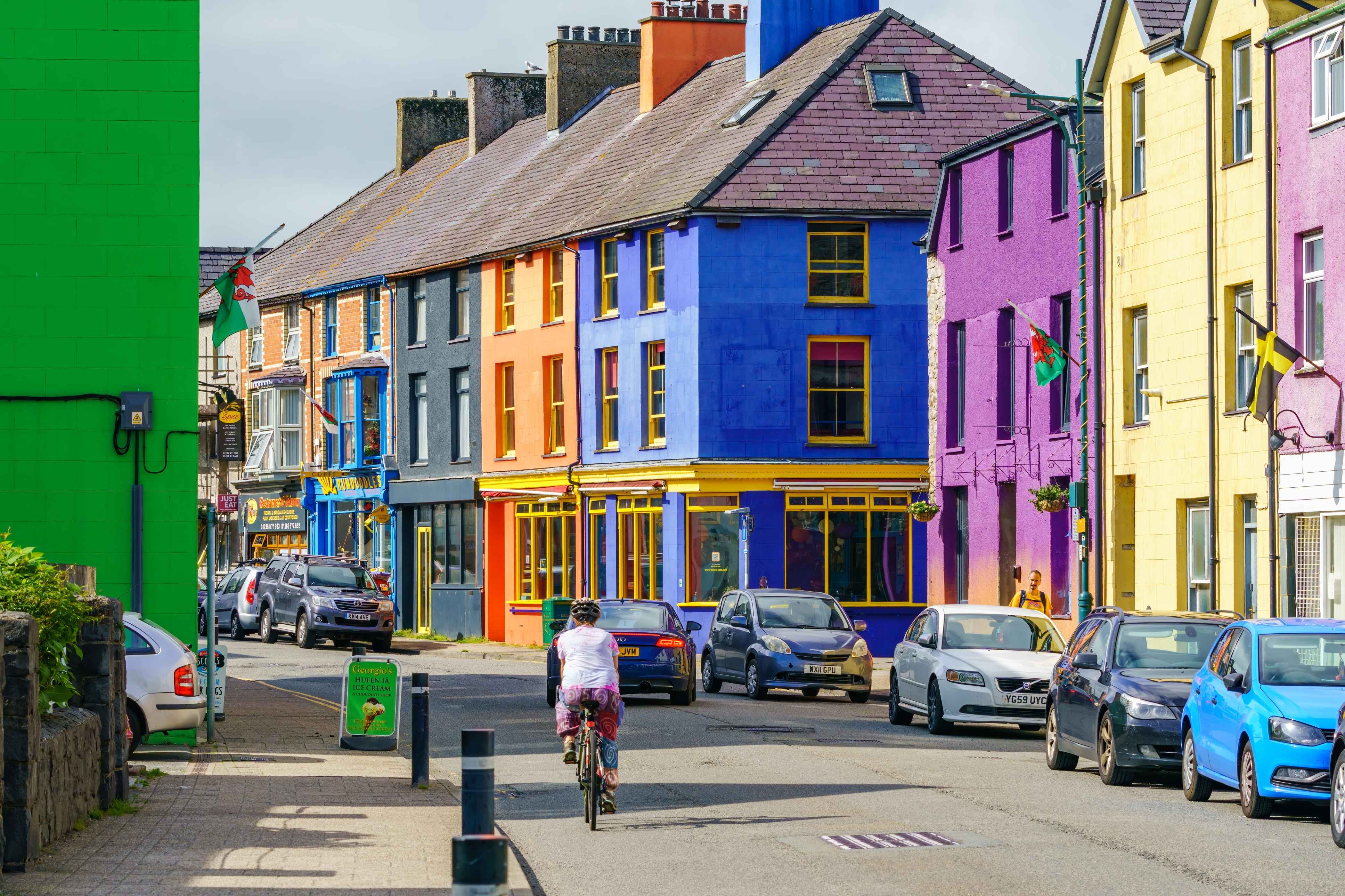 Stryd Fawr Llanberis sydd ag adeiladau lliwgar a thrawiadol, sy’n gynnwys cymysgedd o dai a busnesau, a cheir wedi'u parcio ar un ochr a beiciwr ar y ffordd