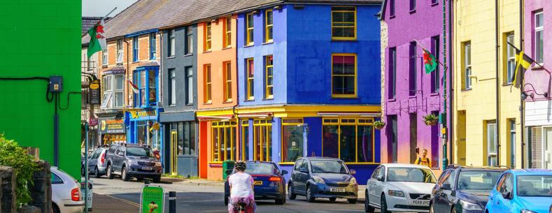 Stryd Fawr Llanberis sydd ag adeiladau lliwgar a thrawiadol, sy’n gynnwys cymysgedd o dai a busnesau, a cheir wedi'u parcio ar un ochr a beiciwr ar y ffordd
