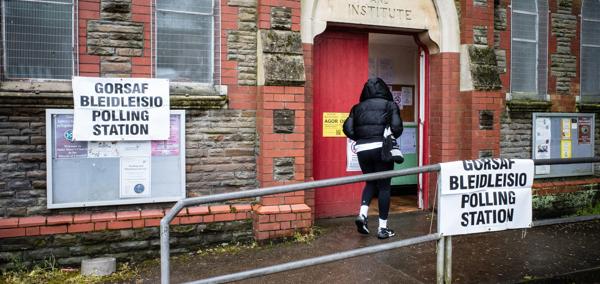 Person mewn côt ddu yn mynd i mewn i orsaf bleidleisio.