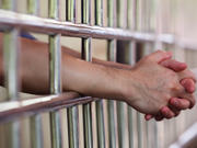 A man’s arm resting on prison cell bars