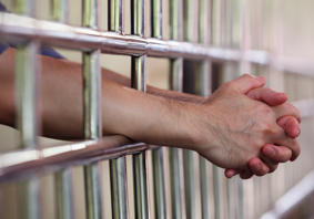 A man’s arm resting on prison cell bars