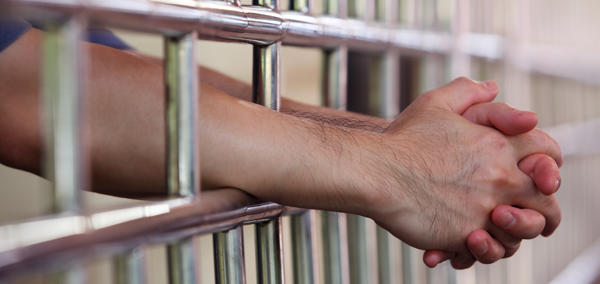 A man’s arm resting on prison cell bars