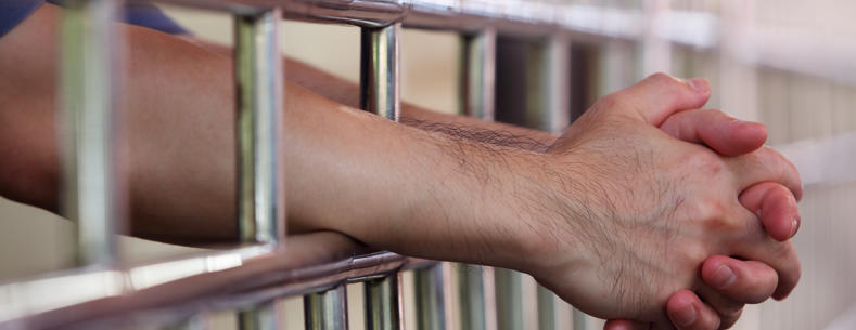 A man’s arm resting on prison cell bars